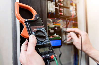 An electrician performing a safety check inspection on a rental property testing a switchboard with a voltmeter