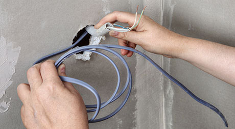 An electrician pulling wires through a hole in the wall installing power outlets