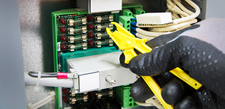 Electrician wearing safety gloves removing a blown fuse to put in a new one