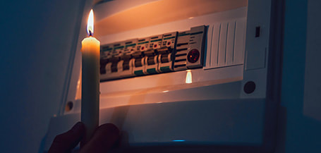 Holding a candle up to an electrical switchboard to see what is wrong because of a power outage